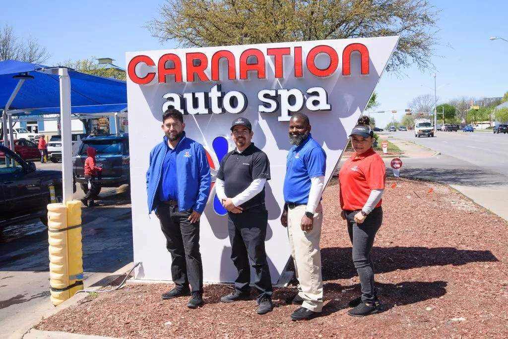 Carnation Auto Spa employees pose in front of a sign displaying the business name. In 2023, Carnation Auto Spa introduced Grazzy cashless tipping options and saw an overall increase in team tips.